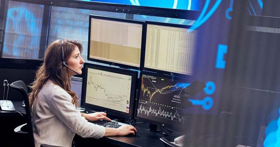 Borsa işlem istasyonunda bir analıstin çoklu monitörlerde finansal grafikleri izlemesi