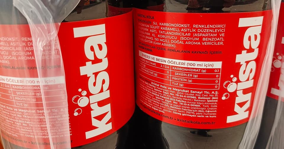 Kristal Kola markasının kırmızı etiketli şişeleri ve ürün bilgisi etiketi yakın çekimde.