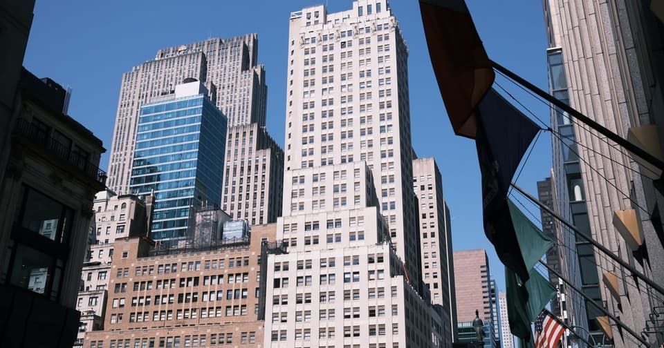 Historic and modern skyscrapers rising on a sunny day, with flags on poles in the foreground