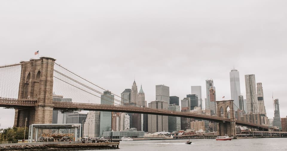 Brooklyn Bridge and the Manhattan skyline rising behind the river under a gray cloudy sky