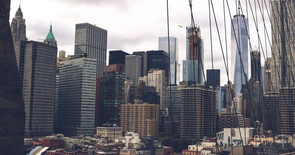 Manhattan skyscrapers lined up in cloudy weather seen through the bridge's steel cables