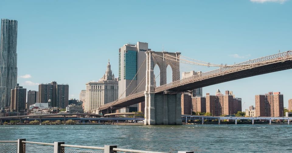 Brooklyn Bridge stretching over the river under a clear blue sky and waterfront buildings