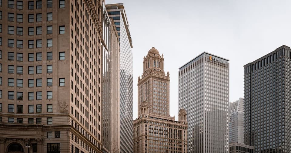 A city where a historic building with an ornate tower stands alongside modern skyscrapers on a cloudy day