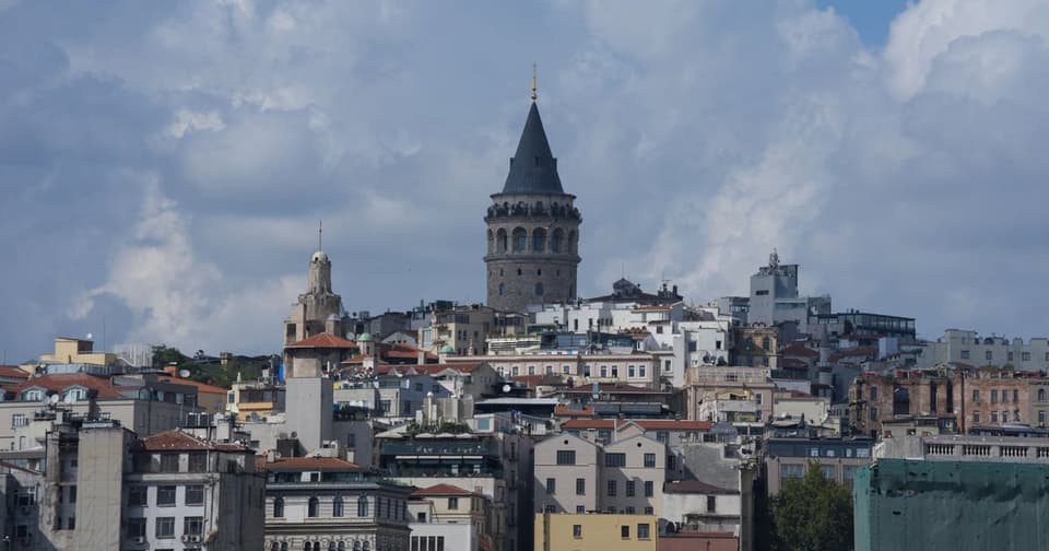 Galata Tower rising above hillside buildings under a cloudy sky